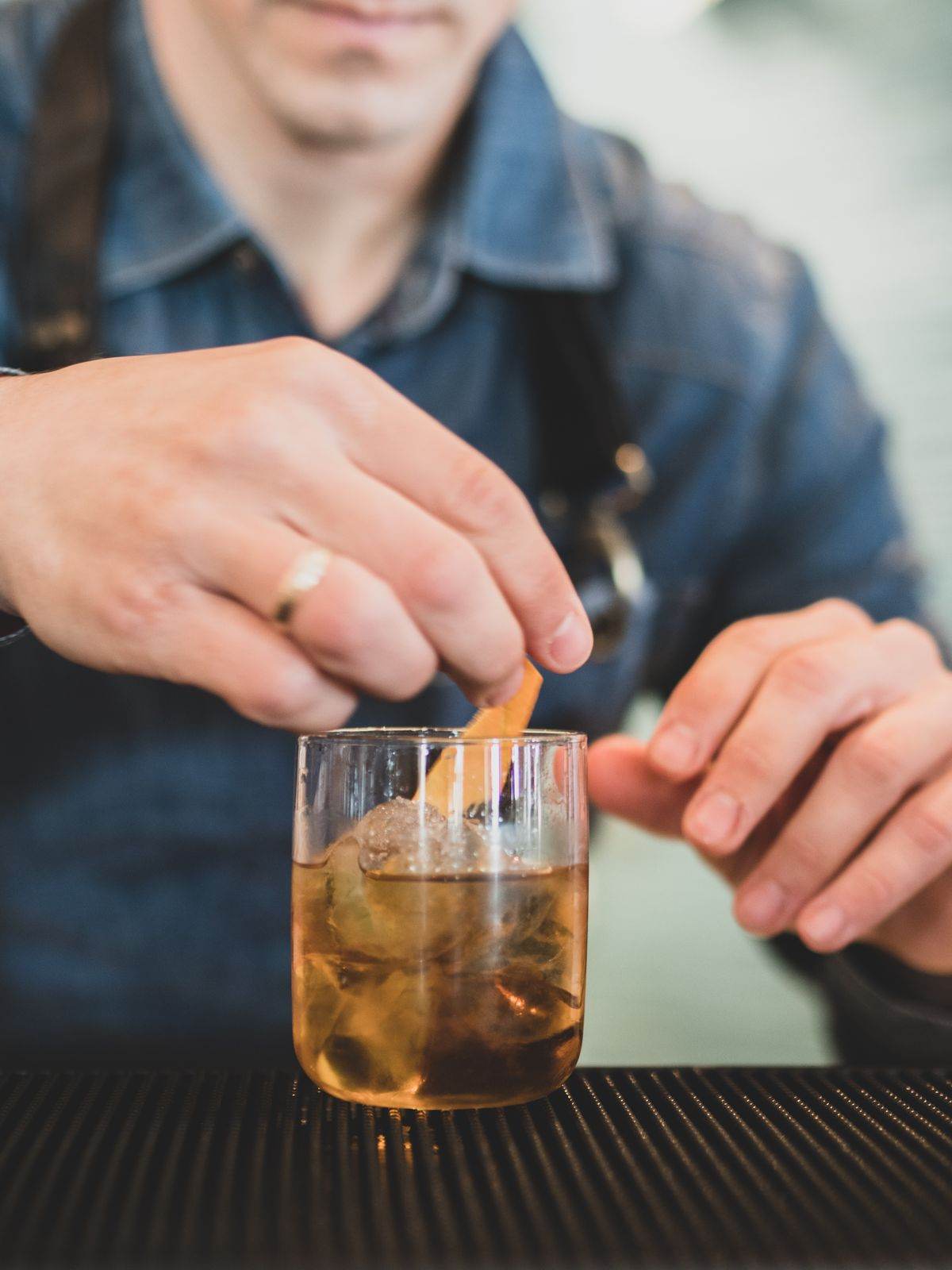 Close-up hands crafting a classic cocktail with ice and citrus peel