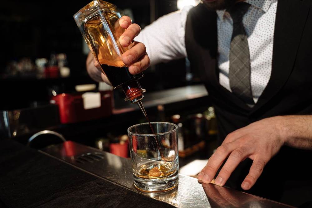 Close-up bartender hands pouring whiskey into a glass