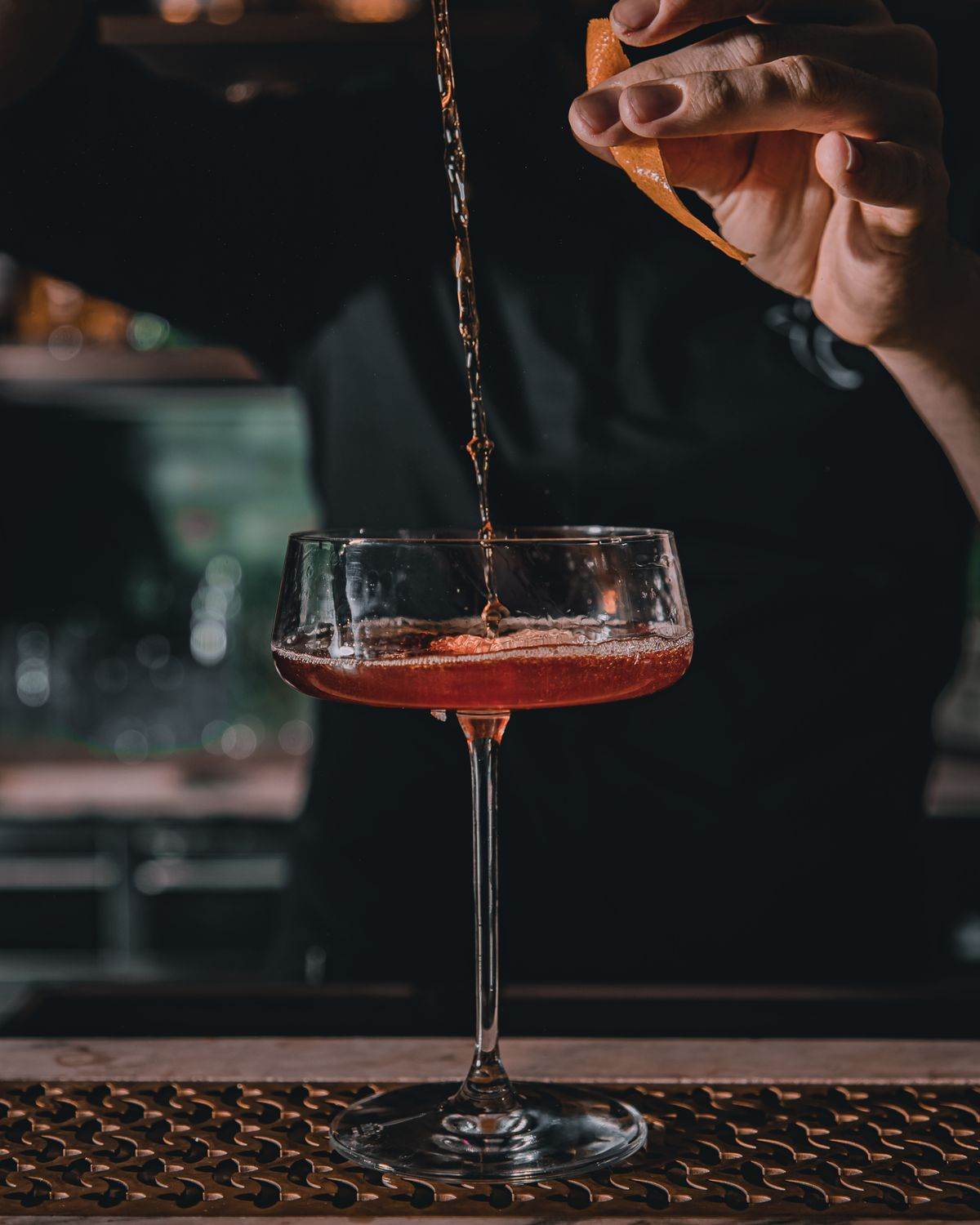 Bartender pouring a cocktail with orange garnish into elegant glassware