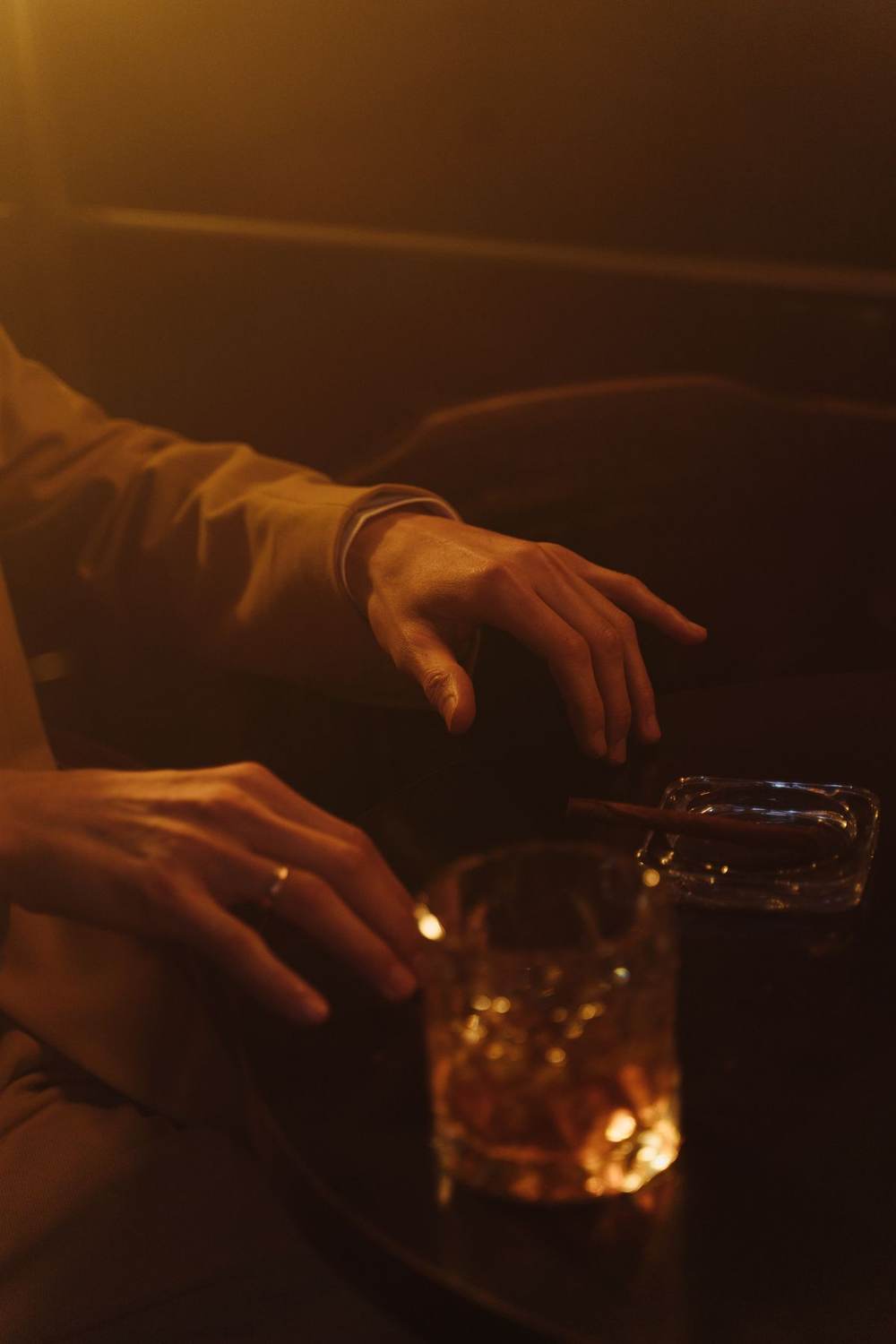Hands beside a whiskey glass on a dark table